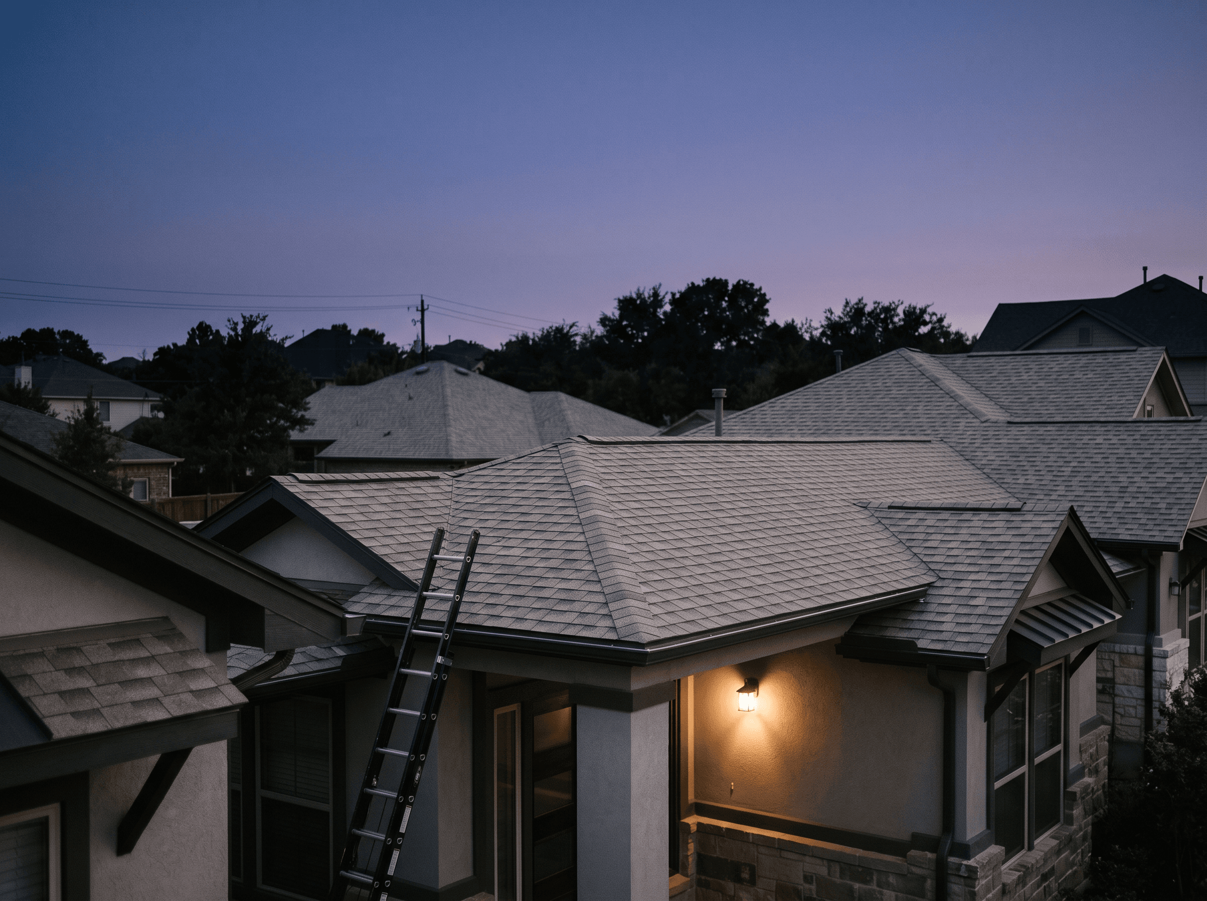 Fresh architectural shingle rooflines at twilight with a ladder against the eave and a warm porch light below